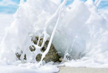 Water crashes around a stone at the sea.